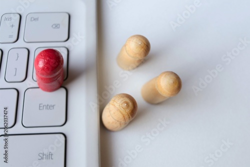 ​A red wooden peg doll standing on a laptop keyboard with natural figures in the background, concept of remote work, digital leadership, and online recruitment.