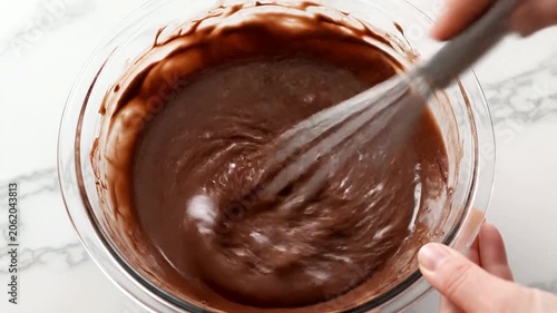 Close-Up Overhead Shot of Hand Whisking Creamy Chocolate Batter in a Clear Glass Bowl for Culinary Use