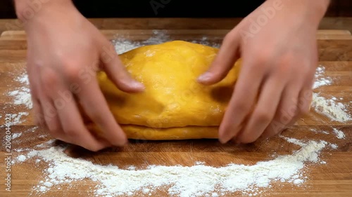 Close Up POV Shot of Hands Kneading Vibrant Yellow Egg Pasta Dough on a Wooden Surface with Scattered Flour for Culinary Preparation