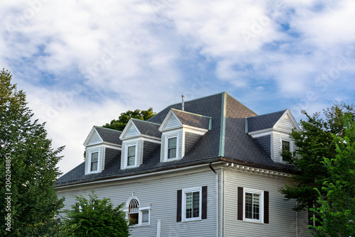 Classic residential house with gabled dormer windows against partly cloudy sky in Brookline, Massachusetts