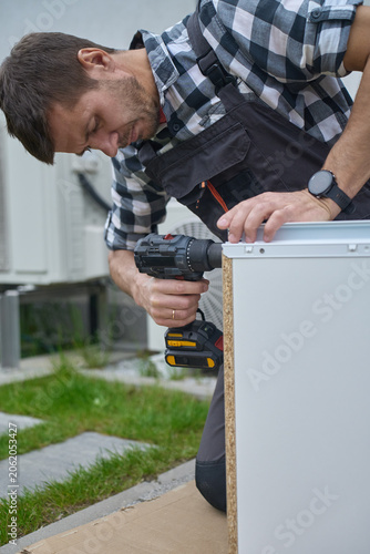 Man secures drawer side with cordless drill while holding the panel steady outdoors