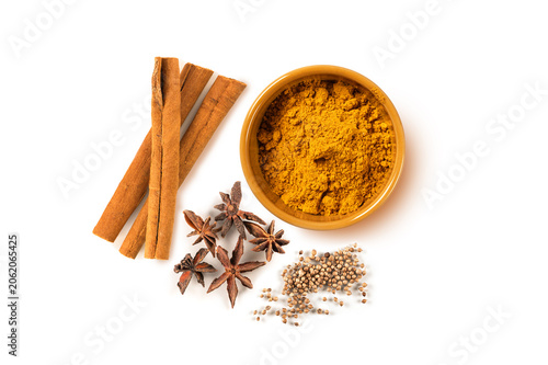 Top-down view of various whole and ground spices including  cinnamon sticks, star anise, coriander seeds, and  golden bowl of curry powder, isolated on white background. Perfect for aromatic recipes.