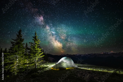 A clear, starry night with the Milky Way in the background, next to a camping tent and the rocky Canadian mountains 