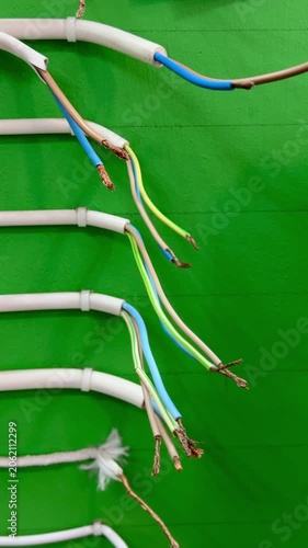 Assorted electrical wires samples on stand, neatly arranged by length and section on green display board, white sheathed cables.