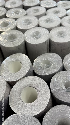 Close-up wallpaper rolls glitter texture, stacked vertically in store showroom, silver metallic finishes catching light, detailed.