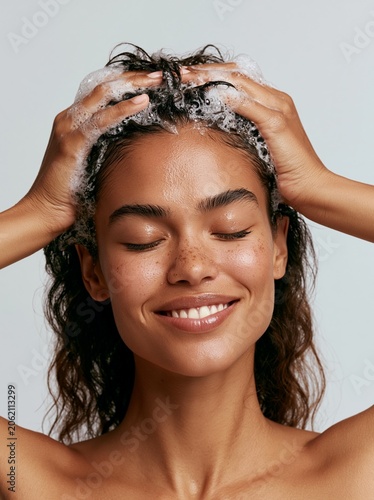 Smiling young Black woman washing her hair with shampoo foam