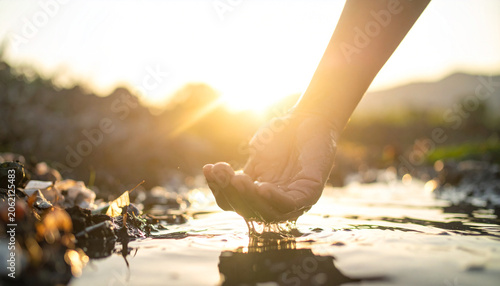 Hope in Hand: A hand cups shallow water as the sun sets, casting a warm, hopeful glow over the scene, symbolizing resourcefulness and the preciousness of life's essentials.
