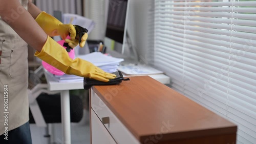 Cleaning lady disinfecting wooden furniture in the office