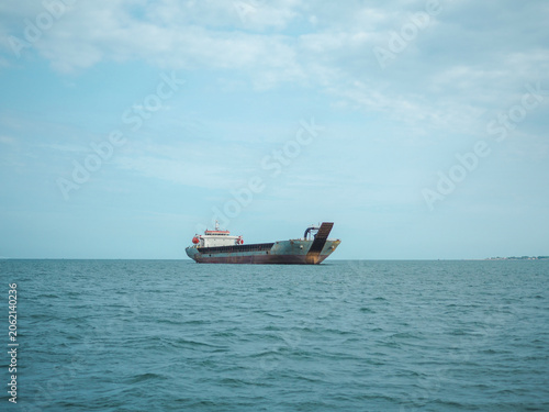 Fotografía A cargo ship sails across the calm blue sea under a vast sky with scattered clouds, representing a journey of trade and transport