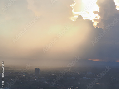 Industrial smog or burning waste pollutants drift into the air, affecting the atmosphere and the sun. Buildings and trees obstruct the view, reducing visibility.