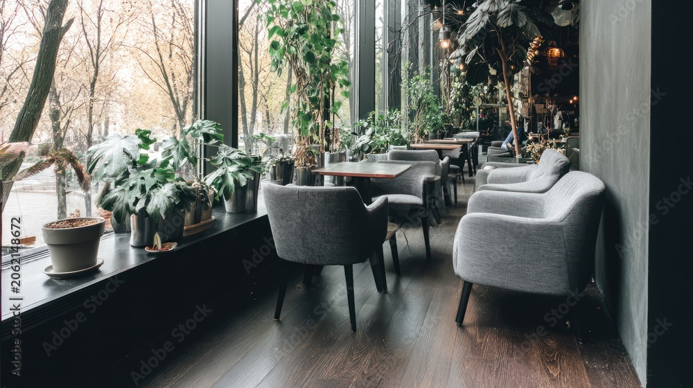 Fototapeta premium Indoor cafe with plants and comfortable seating near window