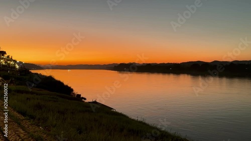 A beautiful wide landscape panning shot of vibrant orange sunset golden hour over Mekong River in Chiang Khan, Thailand 