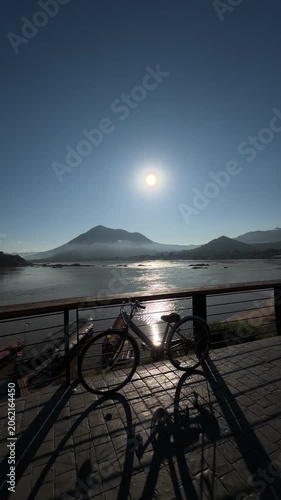 Vertical silhouette bicycle on riverside promenade at sunrise