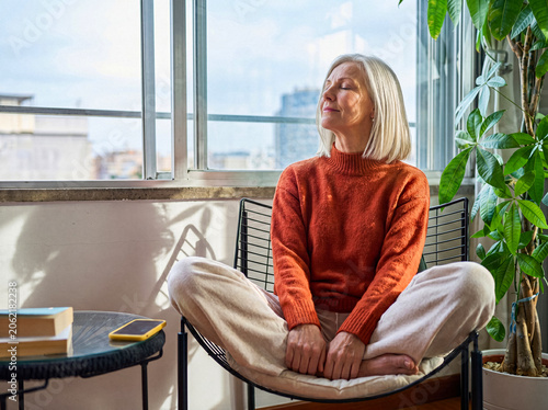 Foto Content senior woman with closed eyes enjoying warm sunlight indoors, meditating or relaxing in peaceful home