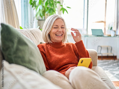 Foto Happy mature woman with grey hair enjoying leisure time at home, laughing cheerfully while using a mobile phone