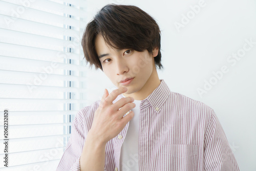 窓際に立つ縦縞のシャツを着る若い日本人男性のポートレート