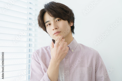 窓際に立つ縦縞のシャツを着る若い日本人男性のポートレート