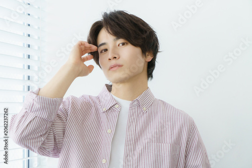 窓際に立つ縦縞のシャツを着る若い日本人男性のポートレート