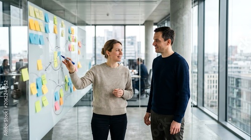 Dynamic professional man and woman discussing project ideas on a glass whiteboard with sticky notes, portraying collaborative office brainstorming