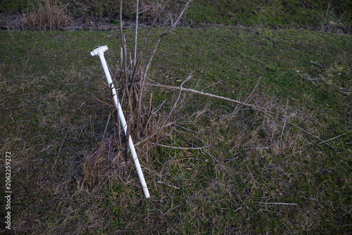Fotografie Abandoned white plastic pipe lying in a grassy field near natural vegetation
