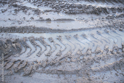 Close-up view of deep tire tread marks left in wet muddy ground. Detailed texture of soil deformation caused by heavy vehicle movement in off-road or construction conditions