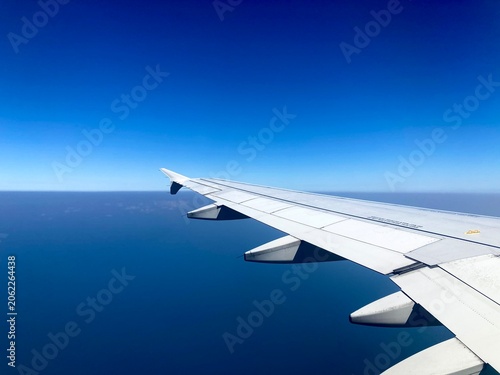 airplane wing flying high above deep blue ocean under a clear sky