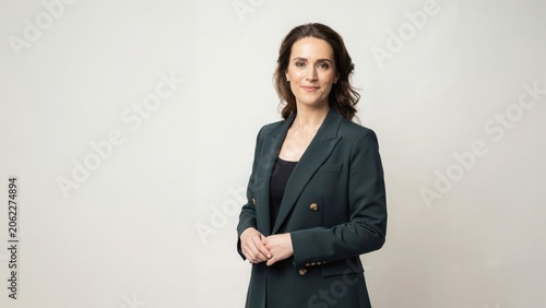 Professional caucasian woman in dark green blazer standing against white background smiling softly.