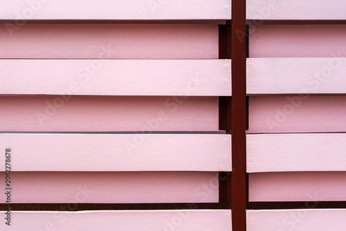 Pink wooden louver fence texture background with brown metal frame. Modern architectural privacy screen made of pink horizontal artificial wood slats installed on dark brown steel frame structure.