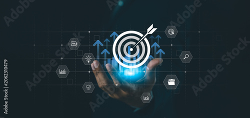 A hand holds a glowing target icon with arrows pointing upwards, surrounded by various technology and business-related icons on a dark background.