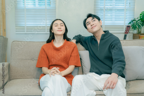 Fotografie A happy young Asian couple sits together on a sofa at home