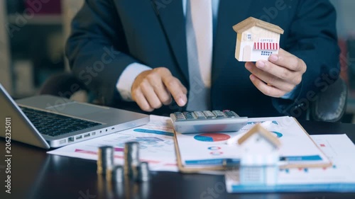 Businessman holding a coffee shop model while using a calculator to calculate business investment costs.