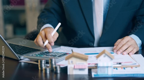Businessman analyzing financial charts, counting coins, and using a calculator to evaluate asset sales and profits.