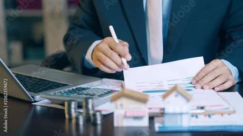 Businessman analyzing financial charts, counting coins, and using a calculator to evaluate asset sales and profits.