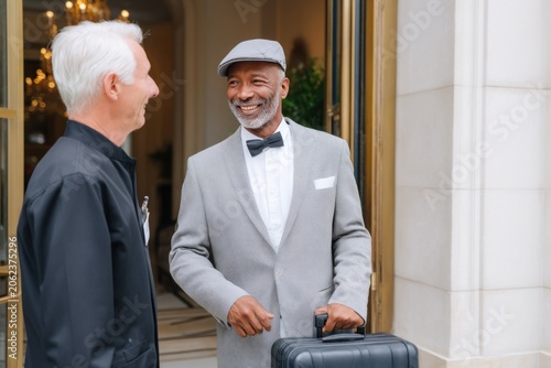 Hotel doorman greeting elegant senior businessman with luggage