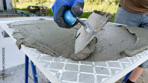 Construction worker applying cement mixture with trowel on tile surface outdoors