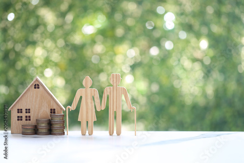 Couple wooden figures standing with a miniature house and coins, representing retirement home planning, property investment, real estate for seniors and financial security for old age.