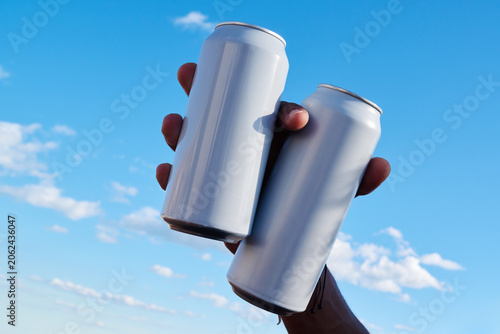 Hand holding two cans against sky