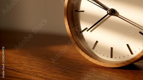 Wooden clock ticking on a desk showing the passage of time in sunlight