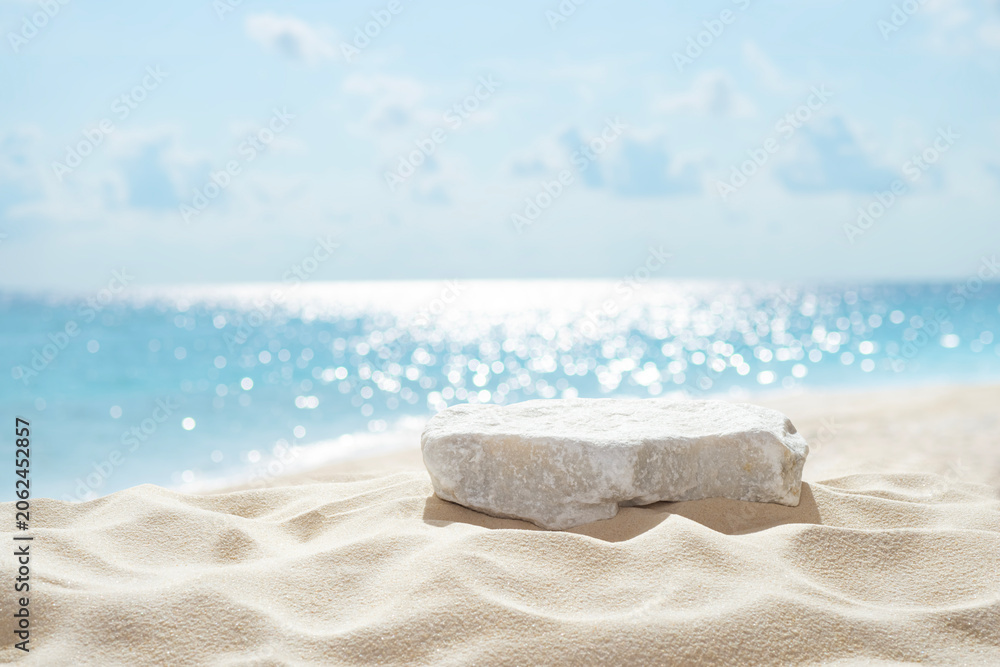 Obraz premium Tropical stone podium on summer beach sand with blurred sunlit sea and sky background