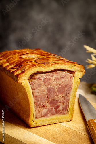 Fotografie Pate en croute or pâté en croûte on a wooden cutting board, aside a knife on a dark gray background
