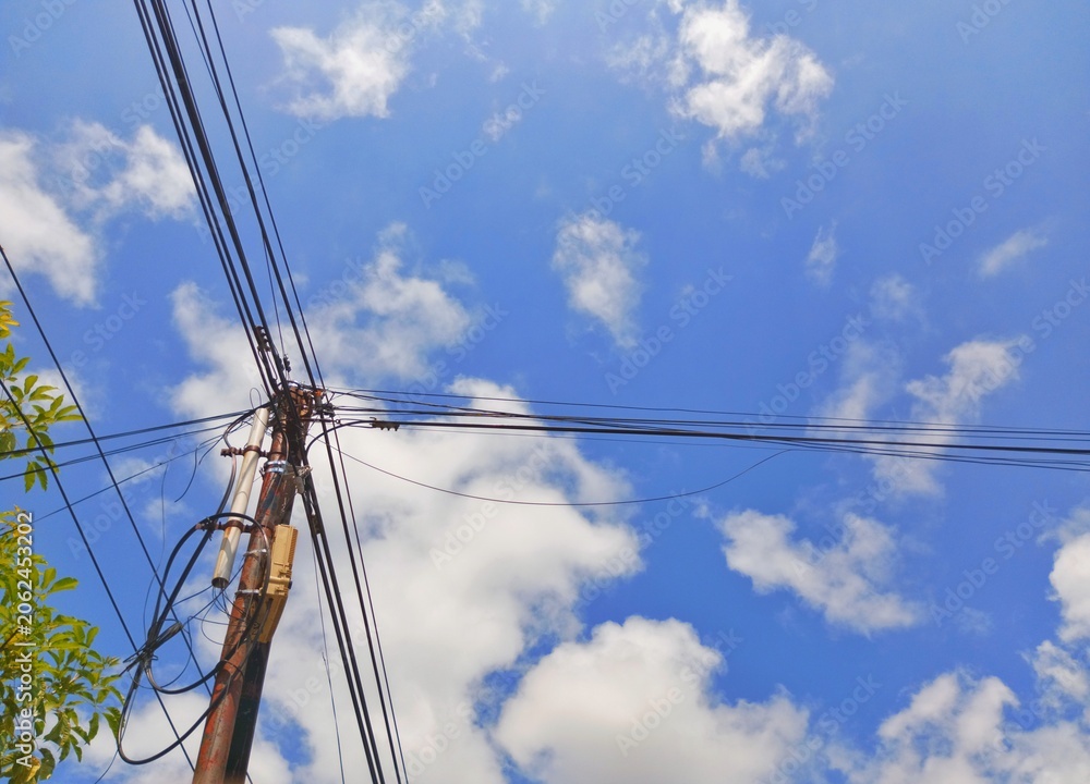 Fototapeta premium Utility pole with tangled power lines against a blue sky with white clouds