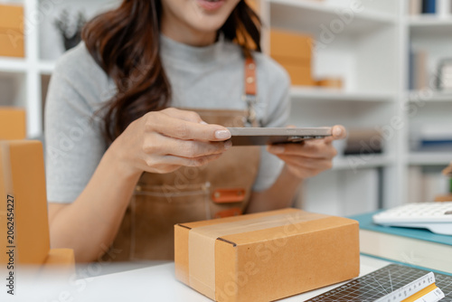 Young entrepreneur managing an online store by processing customer orders, using a laptop, recording parcel details and celebrating successful ecommerce sales in a modern home office.