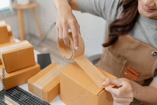 Small business owner packing customer orders, sealing shipping boxes, organizing parcels and managing ecommerce fulfillment in a home office while preparing products for fast and reliable delivery.
