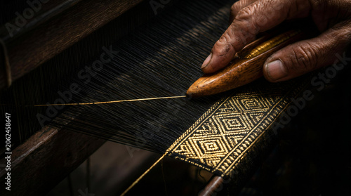 Close up of artisan hands weaving intricate gold and black traditional Thai silk on a wooden loom