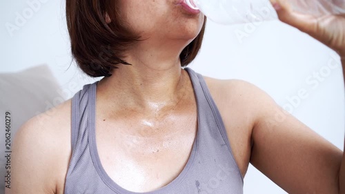 close-up of a sweaty woman in grey activewear drinking fresh water from a plastic bottle after a workout, focusing on hydration, fitness lifestyle, thirst relief, and healthy habits at home