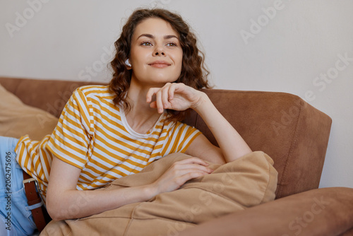 Valokuva A relaxed woman on a sofa at home, wearing a striped yellow shirt, rests her chin on her hand