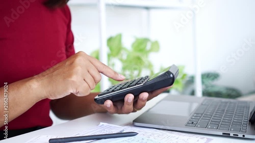 close-up of a woman  using a calculator to manage personal finances, debts, and bills with a laptop and documents on a white desk, focusing on financial planning