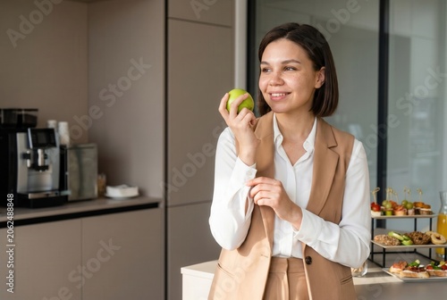Young woman standing in a modern office pantry, choosing a healthy fruit snack