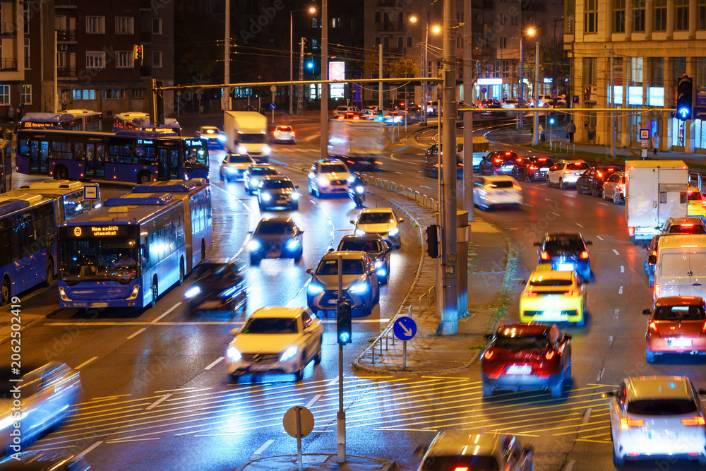 Obraz premium Urban night traffic flow in Budapest featuring cars, buses, and illuminated city streets with motion blur effect.