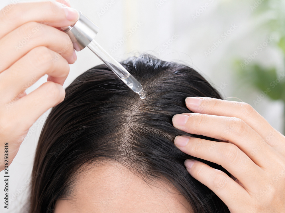 Naklejka premium Woman Applying Scalp Treatment Serum with Dropper for Hair Care